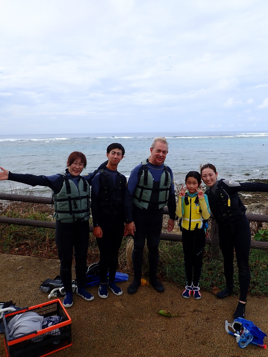 海岸沿いの柵を背景に、ライフジャケットを着用した大人と子供が笑顔でポーズをとる