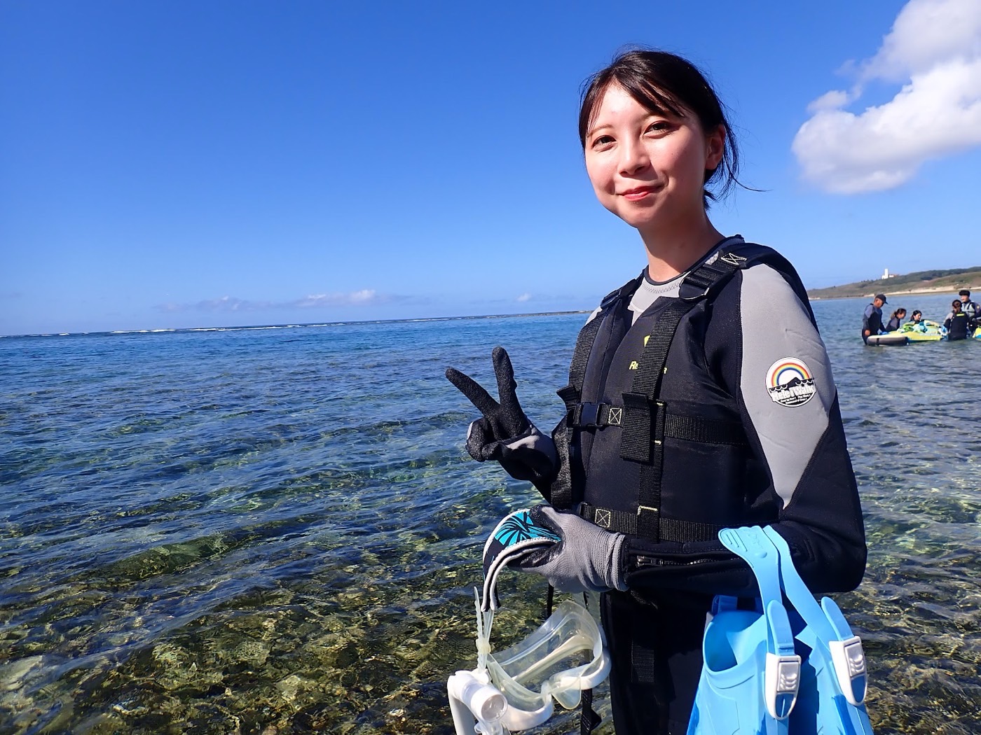 天然水族感で紹介する、晴れた海岸線でウェットスーツを着てシュノーケル器材を持つ女性、天然水族館の雰囲気