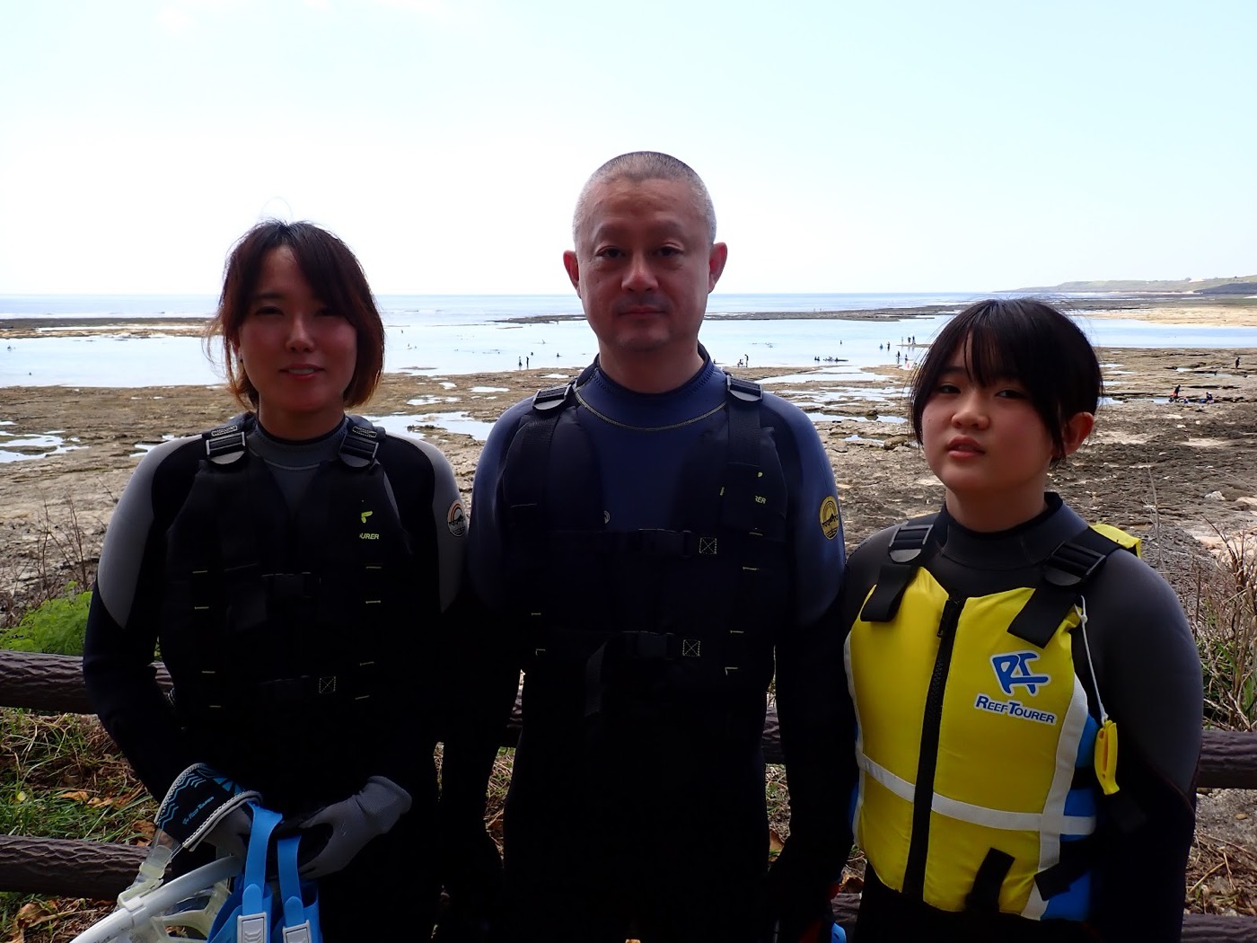 天然水族感で紹介する、海岸の柵を背景に、ウェットスーツを着た大人と小さなお子様のグループ写真
