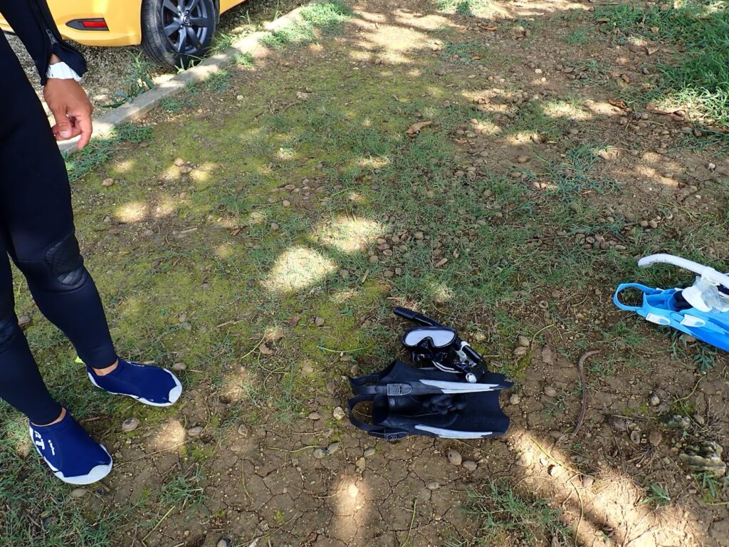 地面に置かれたフィンとシュノーケルセット。準備をするウェットスーツ姿の足元